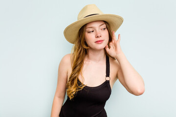 Young caucasian woman going to the beach isolated on blue background trying to listening a gossip.