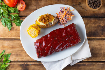 ribs grilled with BBQ sauce and caramelized in honey with baked potato, corn and coleslaw salad. Wooden background