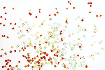 Many small red, green and blue shimmering decorative shiny stars shining on a white surface. View from above. Concept of celebrating Christmas or other holiday. Copy space for text.