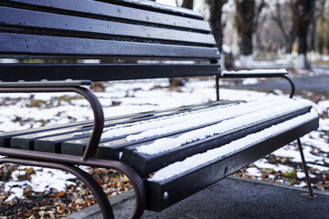 The first snow lies on the park bench at the beginning of winter