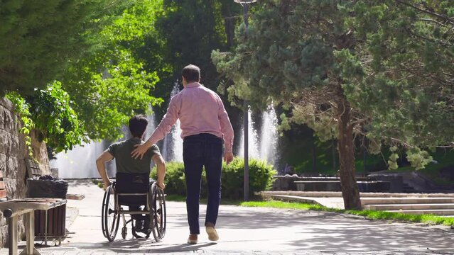 Disabled teenager is driving his wheelchair and walking with his friend.
He is accompanied by his physically disabled young friend walking on the street.
