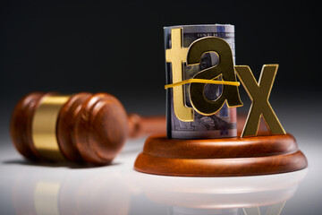 Judge's gavel with dollars in roll with single word tax  against gray background