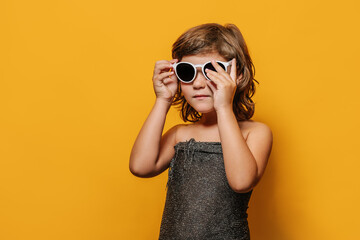 elegant kid puts on sunglasses on yellow background, place for text