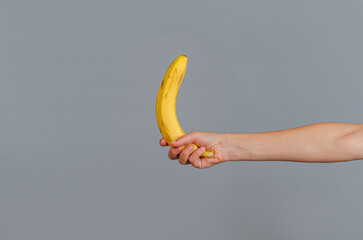 A woman's hand is holding a yellow ripe banana. Gray background.