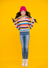 Amazed teenager. Jump and run. Beautiful winter kids portrait. Teenager girl posing with winter sweater and knit hat on yellow background. Excited teen girl.