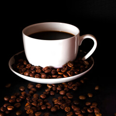 A white cup of coffee stands on the table next to the coffee beans on a black background.
