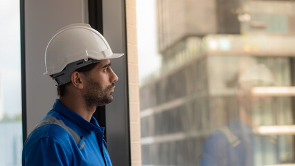 Close-up portrait of a young Caucasian engineer wearing safety workwear standing by the window He...