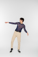 full length of amazed queer person looking away and pointing with hand on grey background.