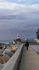 Turista caminando hacia un faro de color blanco y rojo, con cielo cubierto de nubes. Se avecina un...