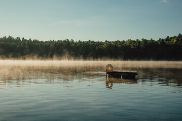 Fototapeta na wymiar Swim platform floating on a quiet foggy lake at sunrise in Ontario, Canada.
