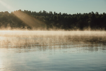 Obraz na płótnie Canvas Morning sun shining on a quiet foggy lake in summer in Ontario, Canada.