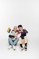 smiling gay man with small lgbtq flags sitting near queer person pointing with finger on grey...