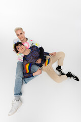 top view of stylish gay man and queer person sitting with lgbtq flags on grey background.