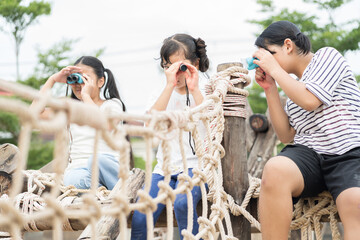 Group of children kids girl exploring nature through magnifying glass and binoculars on outdoor playground. Education, field trips, researcher and discovery concept