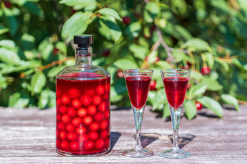 Homemade cherry brandy in glasses and in a bottle on a wooden table in a summer garden