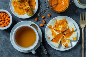 Slices of adyghe cheese poured over sea buckthorn jam with green tea and fresh raw sea buckthorn berries. Healthy breakfast concept