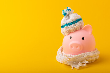 Savings concept. Piggy bank on a yellow textural background. A piggy bank in a warm winter hat that...