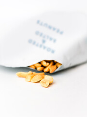 Fototapeta na wymiar Salted peanuts spilling out of a packet. Isolated against white background.