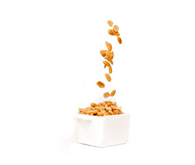 Salted peanuts falling o into a pot full of peanuts.  Isolated against white background
