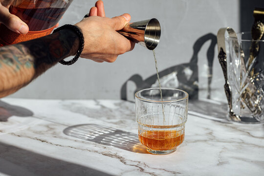 Picture of a person hand pouring whiskey ounce with a jigger on a cocktail glass