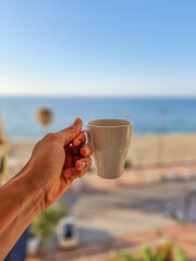 Having a cup of coffee with the sea in the background.