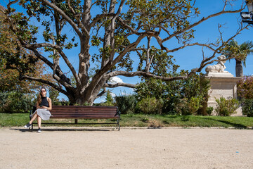 Young woman using sunglasses, sitting on a bench in the park