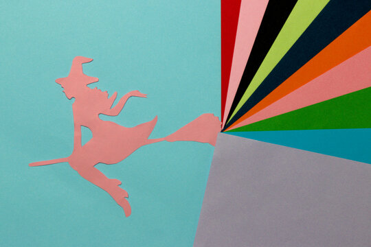 pink paper silhouette of the witch on the blue part of the background, from her broom comes out colorful art part of the background, halloween concept, flat lay, paper craft
