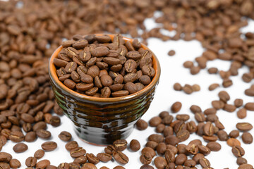 Fragrant roasted coffee beans on a white background and a small cup.