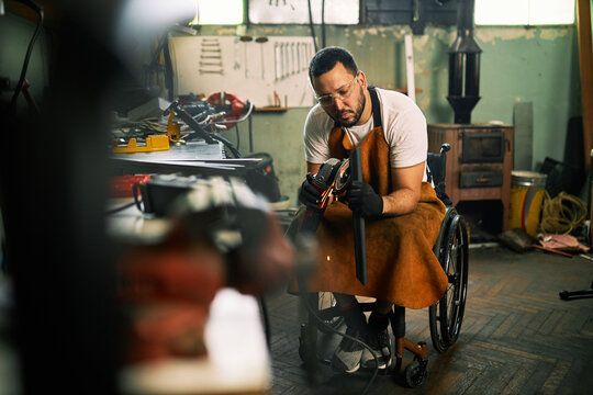 A craftsman in a wheelchair is using grinder in his workshop.