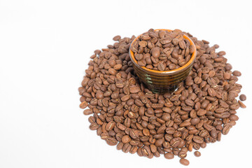 A small saucer with coffee beans stands on a pile of coffee on a white background.