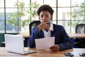 Portrait of attentive male office worker. Serious businessman looking at camera, holding hand on chin and reading document. Paperwork, office work concept.