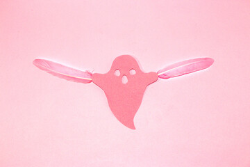 pink ghost with two pink feathers flying on pink background, creative halloween concept, flat lay, paper craft
