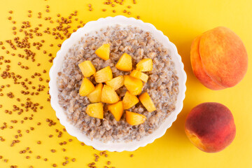 Buckwheat porridge with juicy peach in a white bowl (plate) on a yellow background. Porridge for a child (baby). Healthy breakfast.