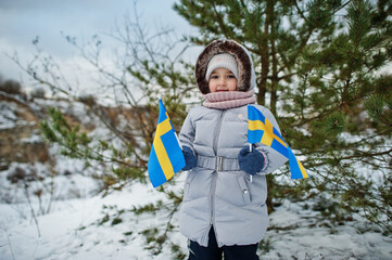 Scandinavian baby girl with Sweden flag in winter swedish landscape.