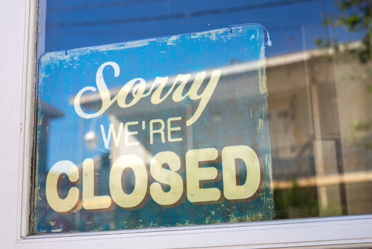 Sign in the shop window behind a pane of glass saying 'Sorry we're closed'. the shop is closed. end of business. closure of business. modern font.