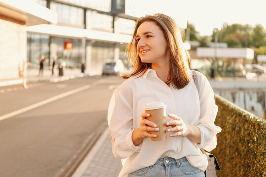 Gorgeous young woman is walking while holding coffee cup on a sunny day.