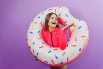 Attractive emotional woman in stylish pink swimsuit with donut inflatable ring on plain background. Beach fashion