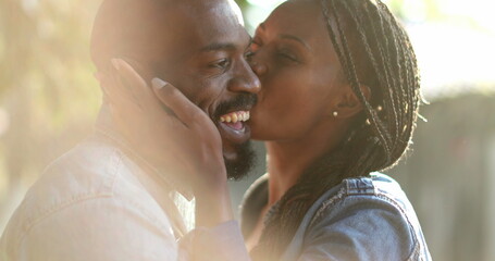 Candid African couple together outside at park. Woman kissing man in cheek outside