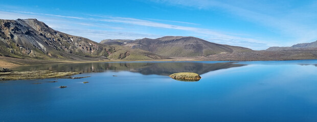 A beautiful landscape in Iceland of mountains, a bright blue and blue sky of light clouds, reflected in  huge flat surface of a reservoir.