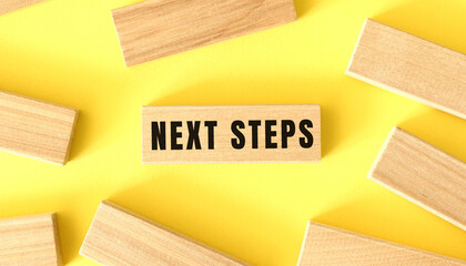 The word NEXT STEPS is written on a wooden blocks on a yellow background.