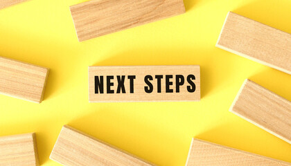 The word NEXT STEPS is written on a wooden blocks on a yellow background.