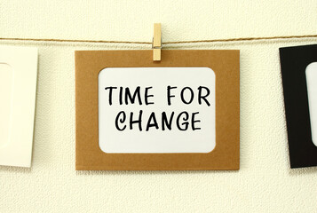 Kraft paper frame hanging on lacing on white wall background. In the frame is written the text TIME FOR CHANGE.