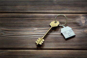Keys with a keychain in the form of a house lie on an old wooden table. The concept of buying, renting, home insurance. Real estate transactions. Space for text.