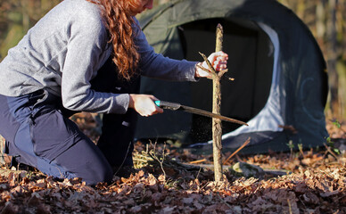 Close up of the hands of a caucasian woman sawing a fallen tree with a hand saw in the forest. Female outdoors collecting wood to start up a fire. Concept of bushcraft and outdoor survival.