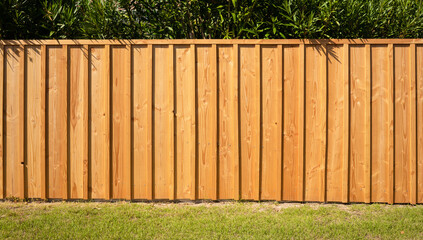 Frontal shot of a wooden picket fence with a green hedge in the background and grass in the...
