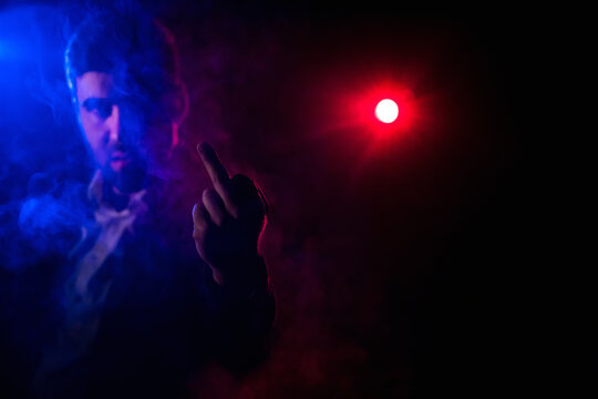 Photo of standing man showing middle finger and pink light on the background.
