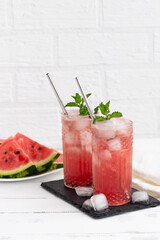 Watermelon smoothie or iced juice with watermelon slices and mint leaf on a white wooden background