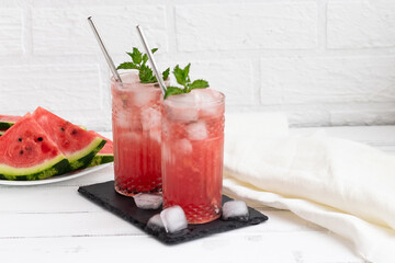 Watermelon smoothie or iced juice with watermelon slices and mint leaf on a white wooden background