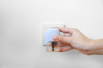 female hand with a fumigator against mosquitoes against the background of a white wall and a socket