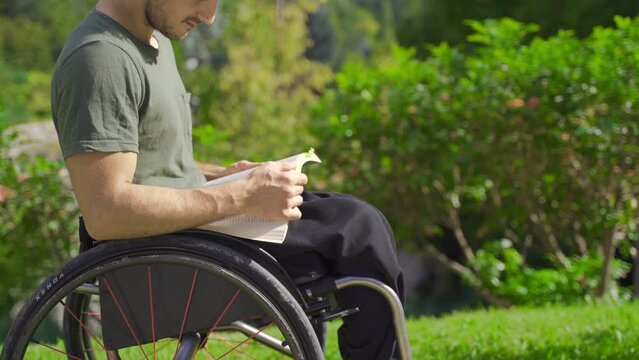 Young man with physical disability is reading a book outdoors.
Disabled teenager in a wheelchair reading a book in a nature park.

